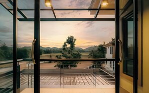 Un balcón con baranda de vidrio que ofrece vistas a un paisaje con árboles y un edificio.