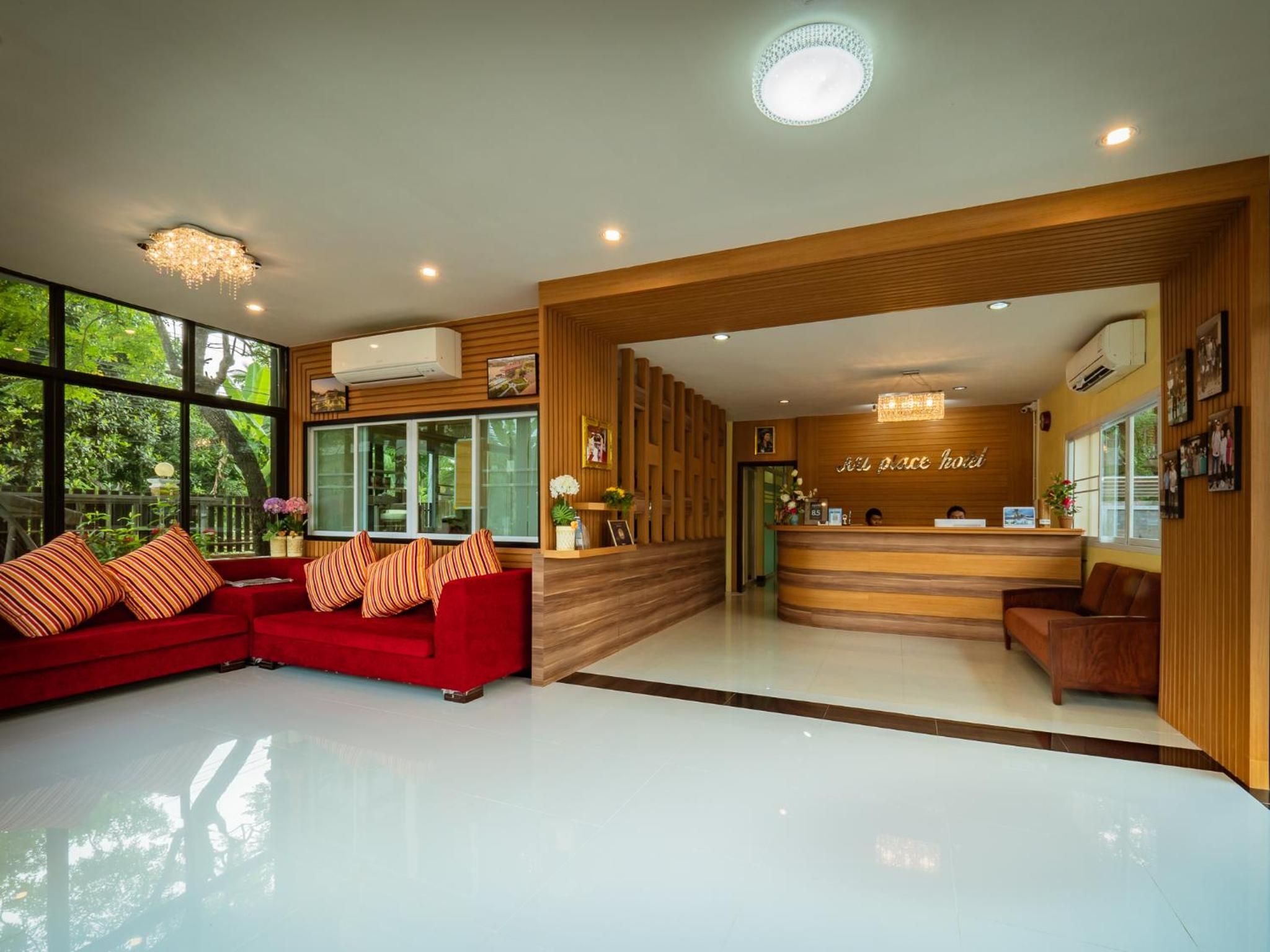 Zona de recepción de hotel con un sofá rojo, mostrador de recepción de madera y ventanas amplias con vistas a zonas verdes.