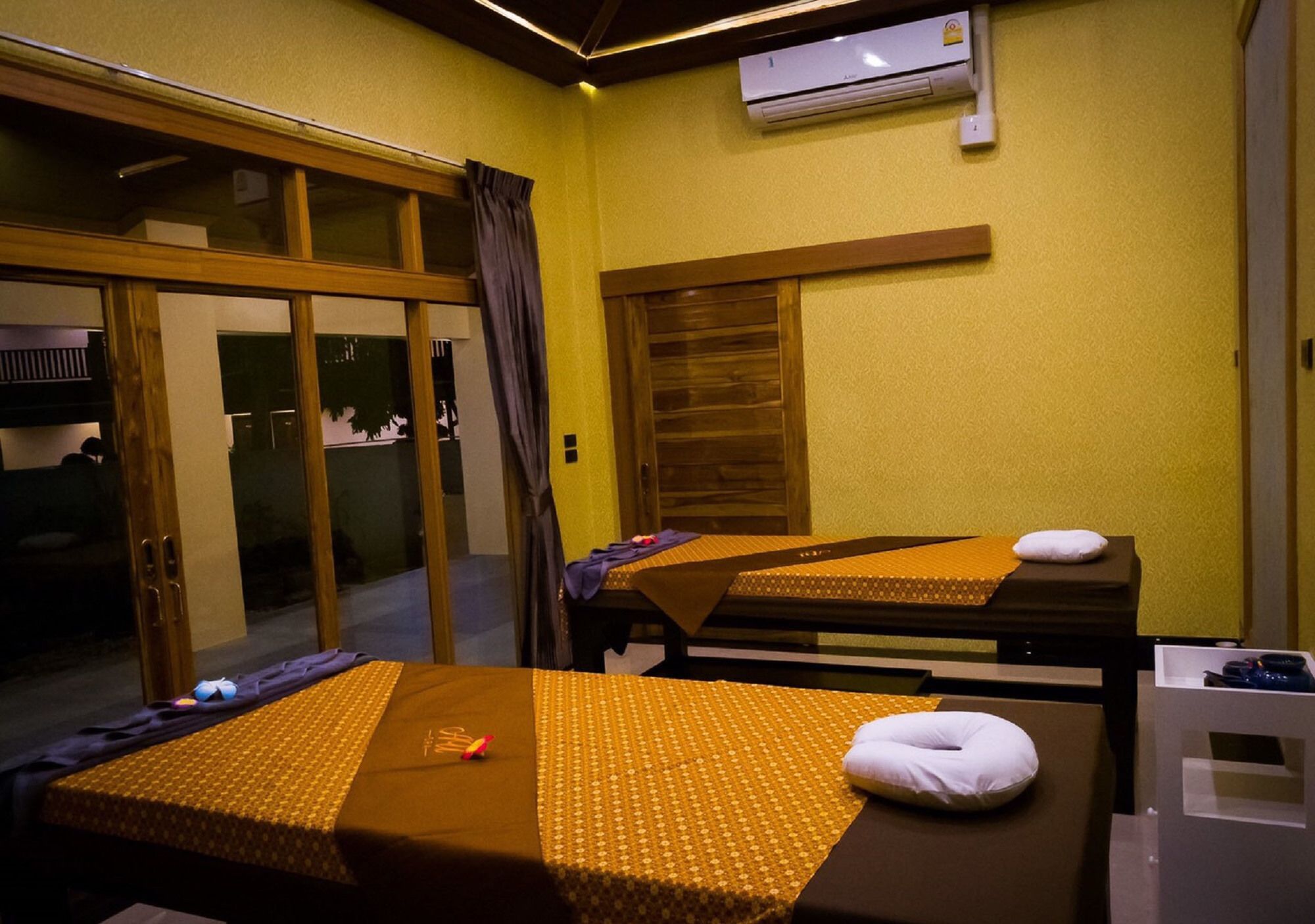 A room with two beds, a sliding glass door, an air conditioning unit, and a small table with a pillow.