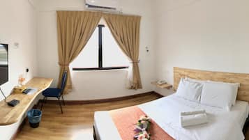 A hotel room with a bed, a desk with a TV, a window with curtains, and a wooden headboard.