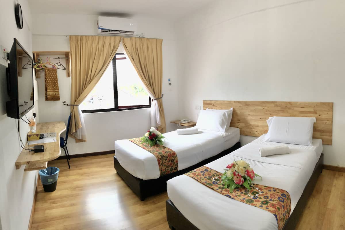 A hotel room with two beds, a wooden desk, a TV, and a window with curtains.