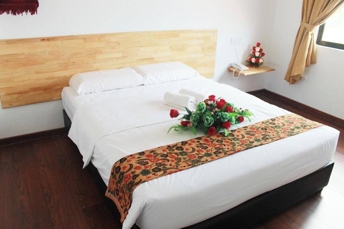A neatly made bed with white linens, a floral bedspread, and a bouquet of red roses.