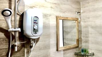 Un bagno con doccetta, termosifone a parete, uno specchio e un ripiano in vetro con articoli da toilette.