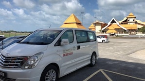 A white van parked in a lot with a building featuring pyramid-shaped roofs in the background. -  AM Transit Inn Kuala Terengganu (Kuala Terengganu)