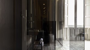 En hotellkorridor med en glasdörr som leder till ett badrum, ett mönstrat golv och en utsikt genom dörren.