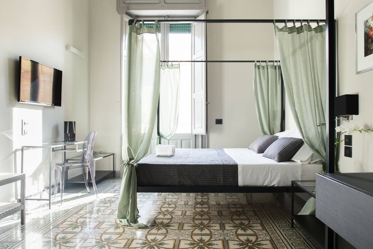 A modern bedroom with a bed, curtains, a TV, and a chair.