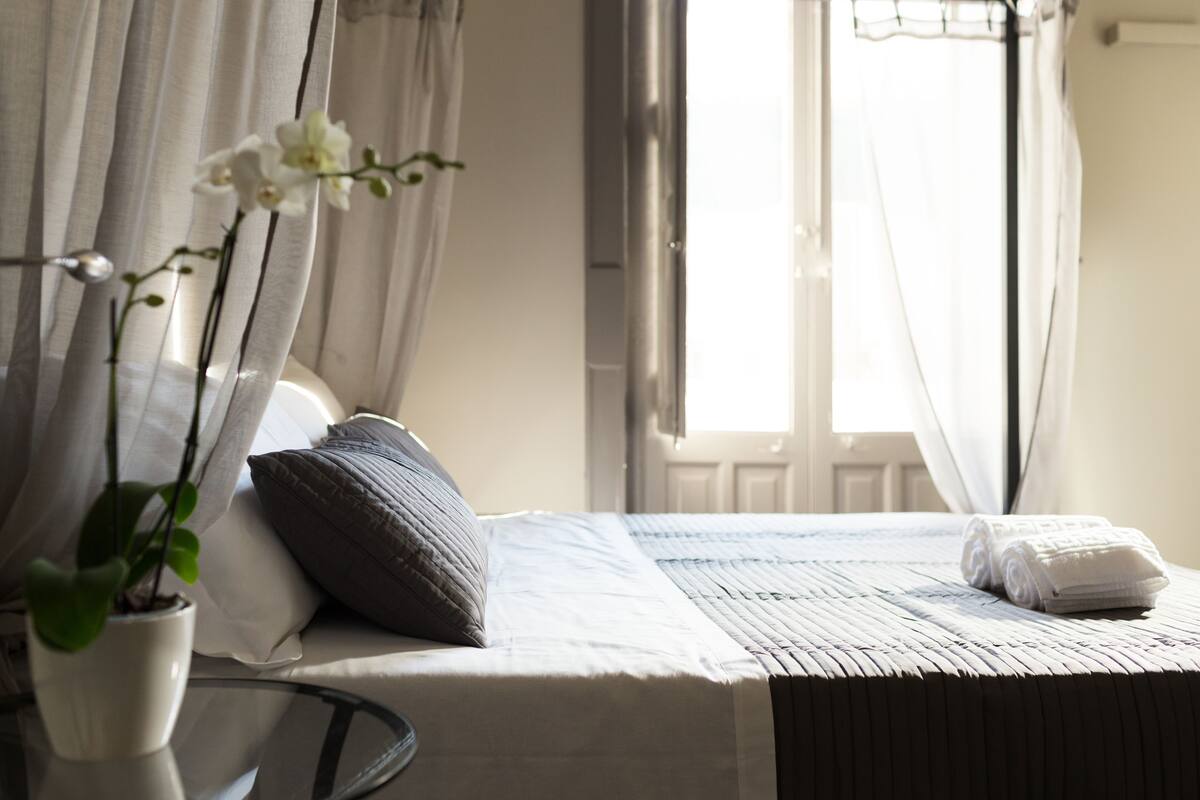 A neatly made bed with a pillow, a rolled towel, and a potted plant on a bedside table.