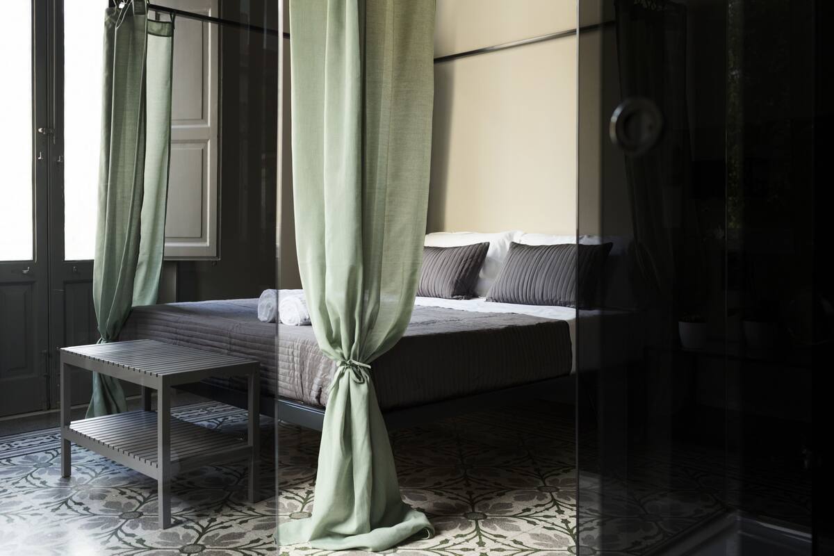 A bedroom with a bed, a bedside table, a curtain, and a patterned floor.