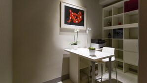 Ett modernt, minimalistiskt rum med ett vitt skrivbord, ett inramat konstverk, en krukväxt och en vit stol.