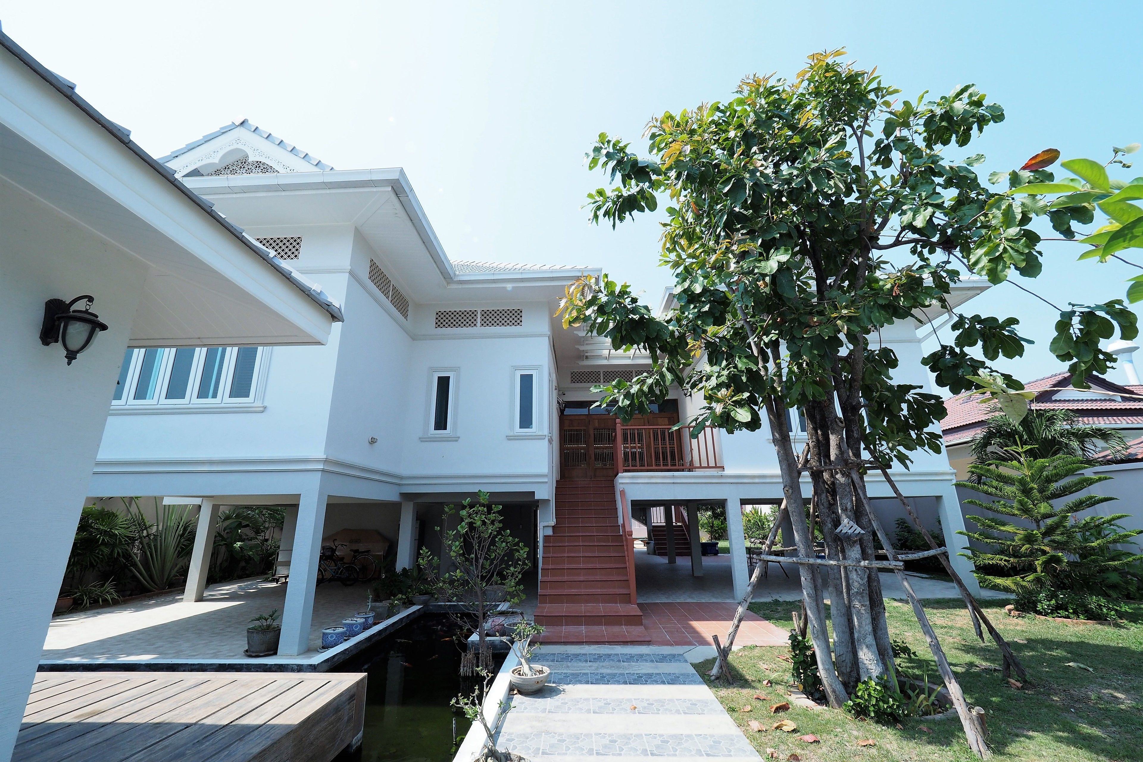 A two-story house with a covered patio, a staircase leading to the upper floor, and a small garden area with potted plants.