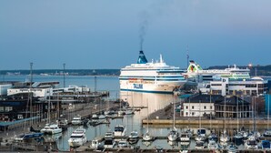 Un vaixell de creuer amarrat en una marina, amb diversos vaixells i edificis al fons.