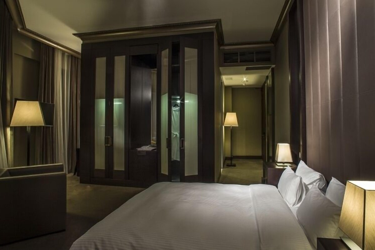 Una habitación de hotel con una cama grande, dos lámparas de noche, un armario y un espejo.