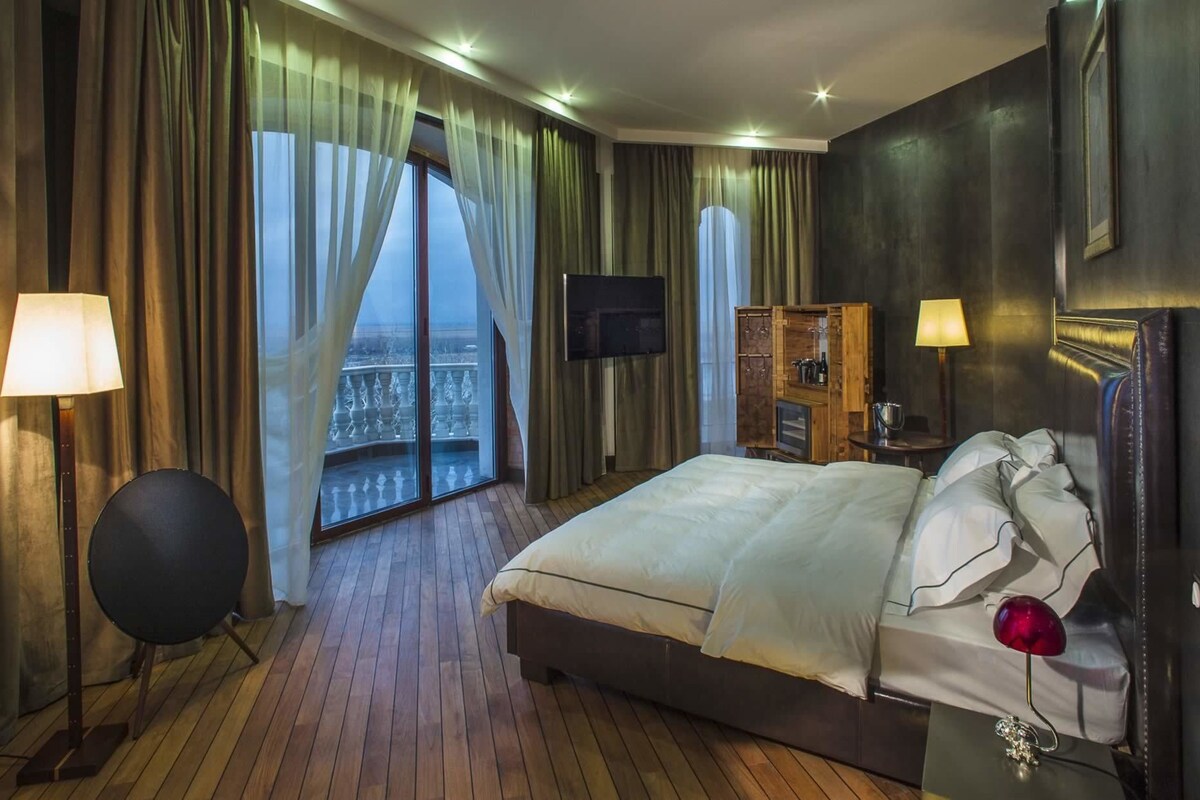 Una habitación de hotel con una cama grande, un televisor, un armario de madera y un balcón con cortinas.