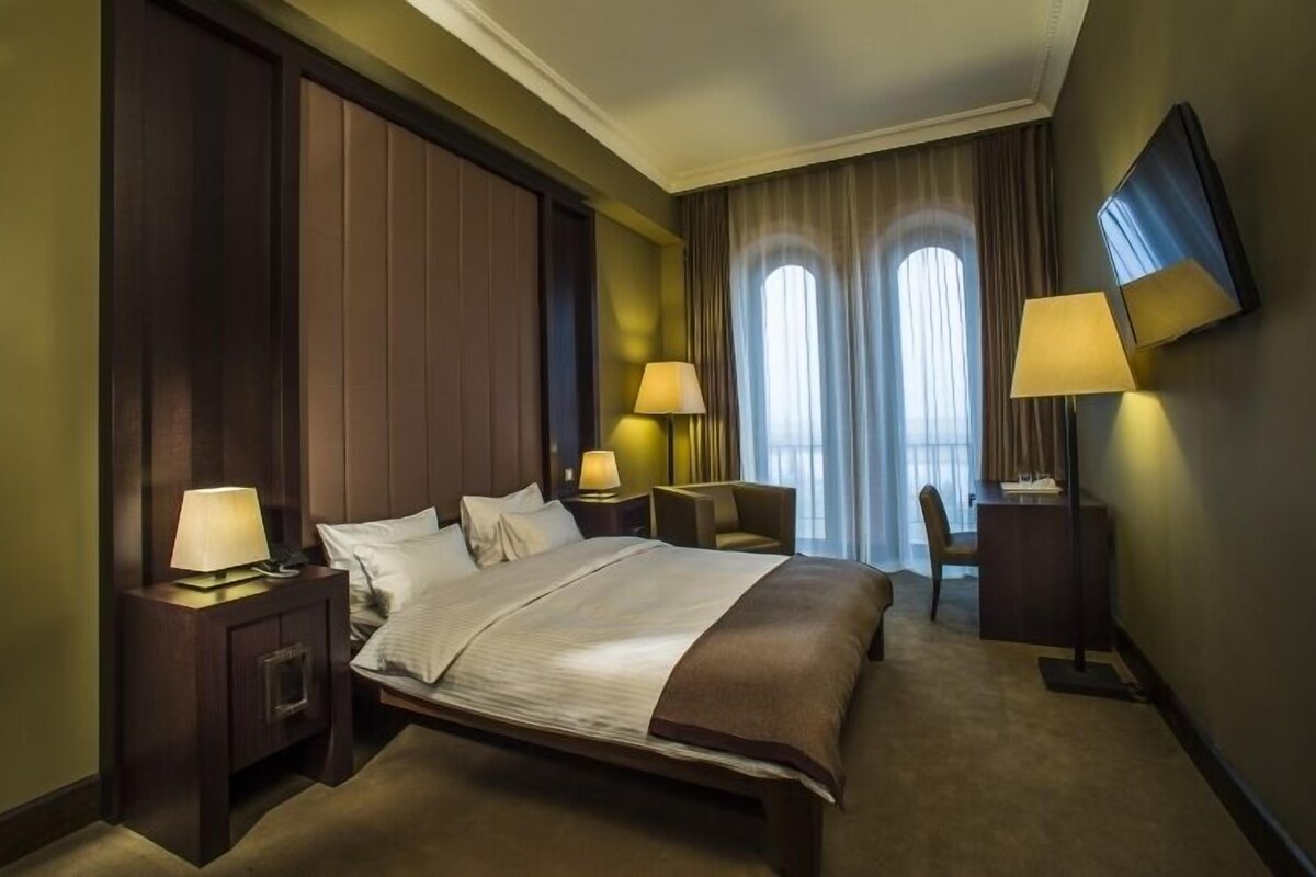 Habitación de hotel con una cama grande, dos mesitas de noche con lámparas, un escritorio con silla y un televisor montado en la pared.