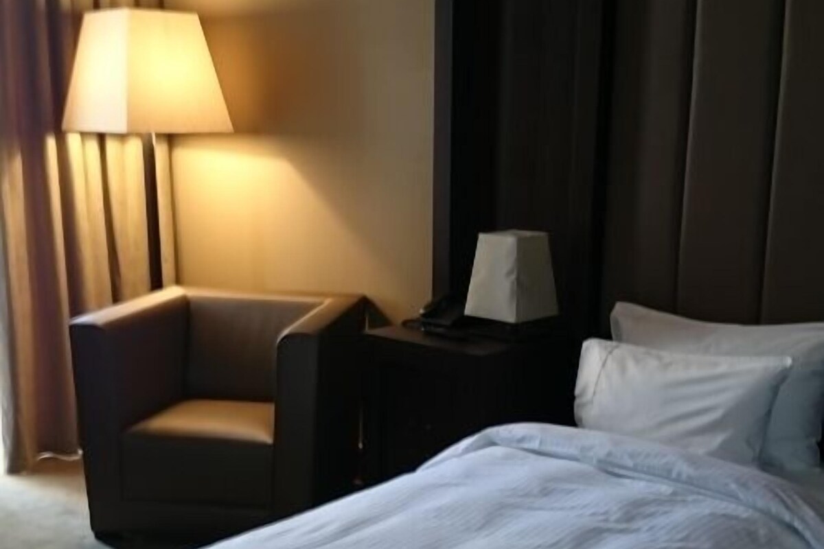 Una habitación de hotel con una cama, una silla, una mesita de noche y una lámpara.