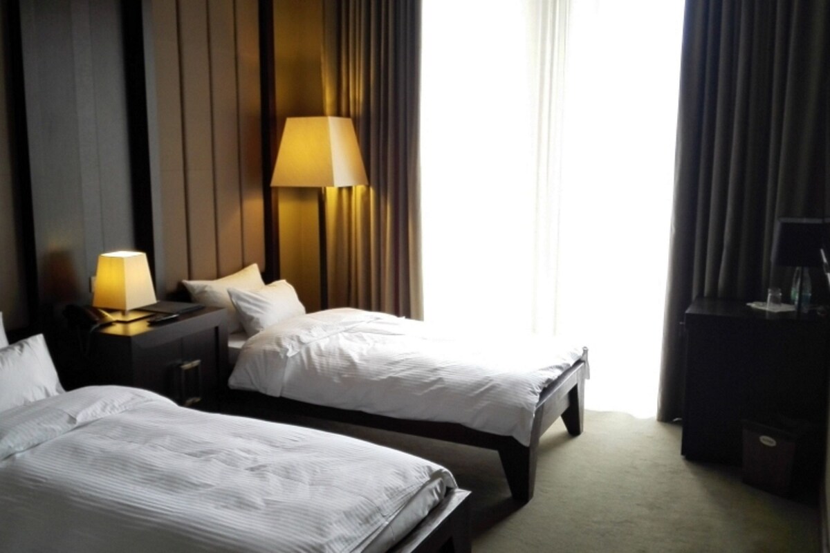 Habitación de hotel con dos camas, una mesita de noche con lámpara, un escritorio con computadora y un televisor.