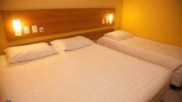Habitación de hotel con dos camas individuales, cabecero de madera y lámparas fijadas a la pared.