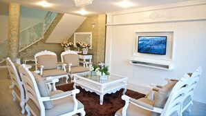 A modern living room with white furniture, a glass coffee table, and a television mounted on the wall.