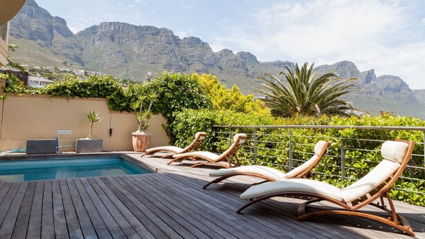 A poolside area with lounge chairs, a pool, and a view of mountains. - Bay Vista Villa (Cape Town)