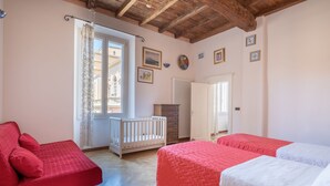 A bedroom with two beds, a crib, a dresser, and a window with curtains.