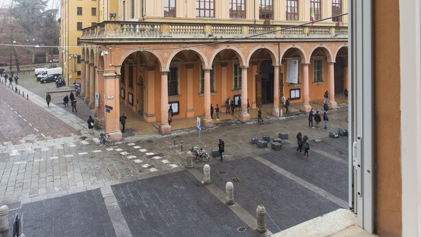A building with a yellow facade and multiple arches, viewed from a window.