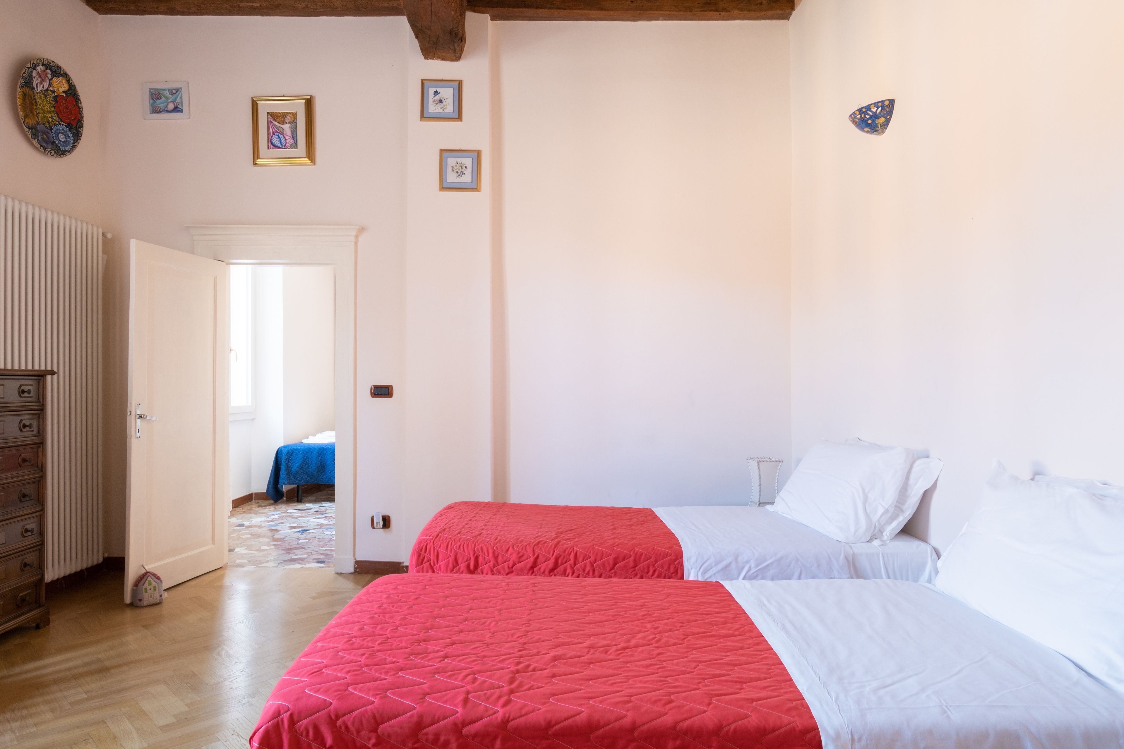 A bedroom with two beds, a dresser, and a door leading to another room.