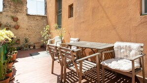 A wooden table and chairs set on a patio with potted plants and a brick wall.