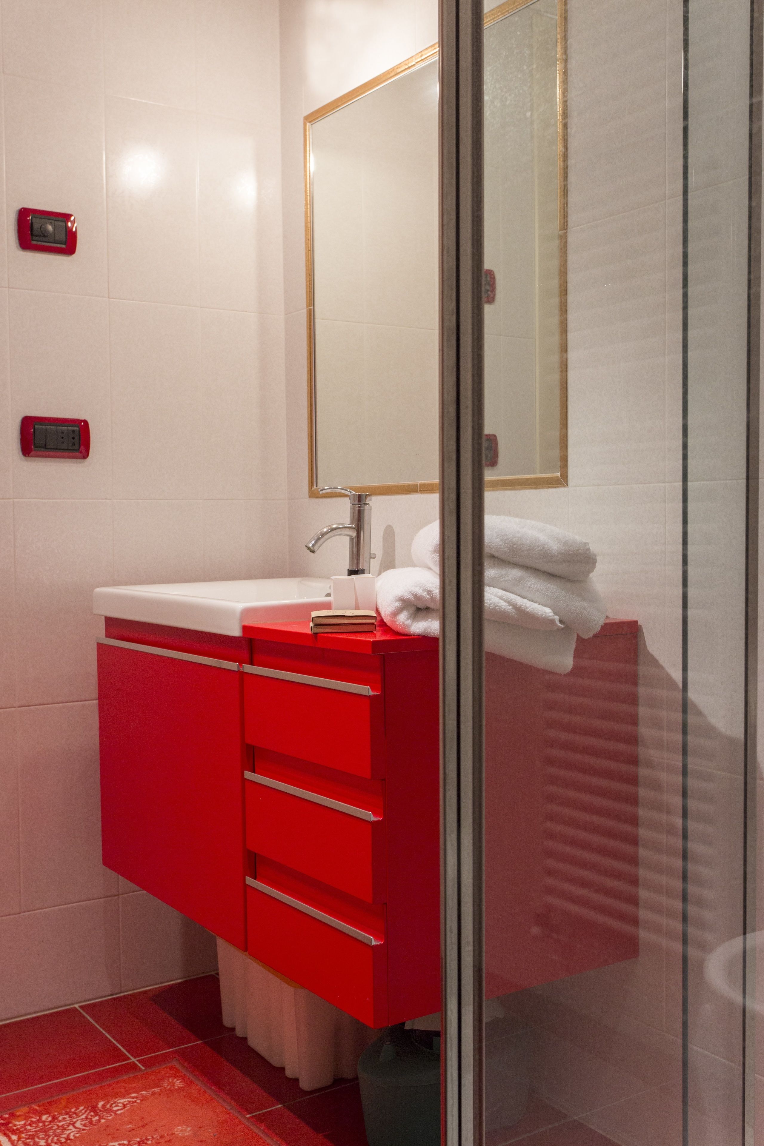 Ein modernes Badezimmer mit einem roten Waschtisch, einem weißen Waschbecken und einer Duschkabine aus Glas.
