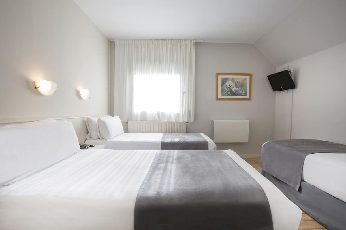 Une chambre d’hôtel avec deux lits, une fenêtre avec des rideaux, un tableau accroché au mur et un téléviseur fixé au mur.