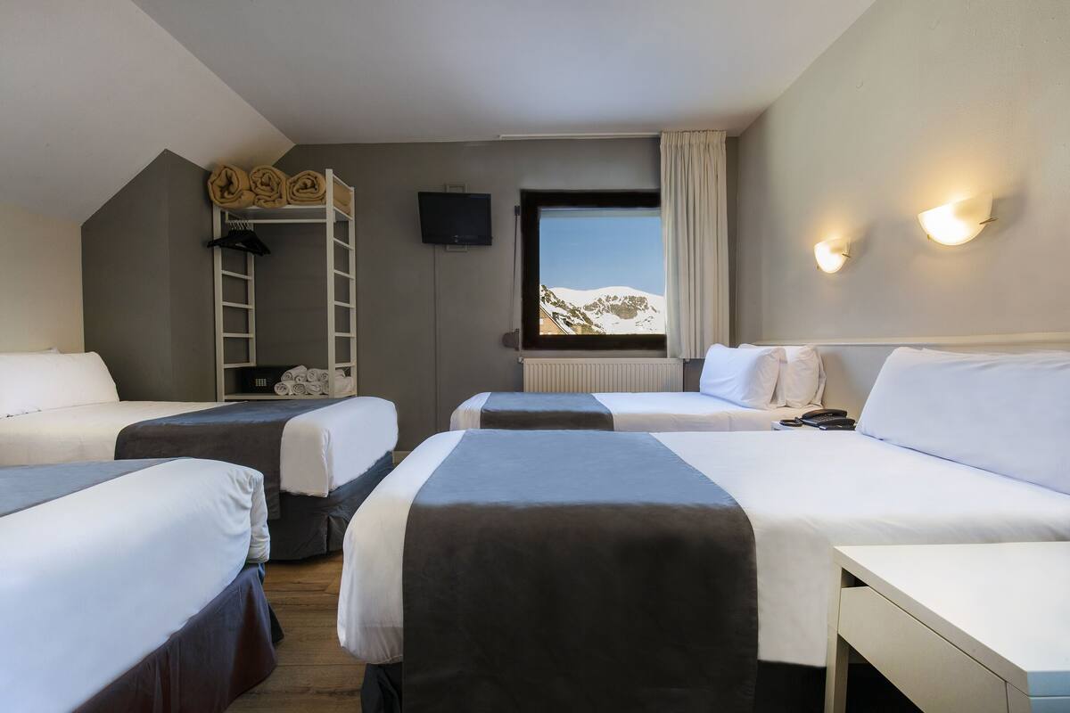 Une chambre d’hôtel avec deux lits, un bureau, une fenêtre donnant sur les montagnes, une télévision et une échelle.