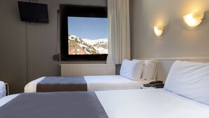 Une chambre d’hôtel avec deux lits, un téléviseur fixé au mur et une vue sur des montagnes enneigées par la fenêtre.