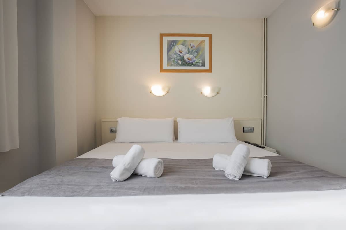 Une chambre d’hôtel avec un lit, deux oreillers, un tableau au mur et deux lampes fixées au mur.