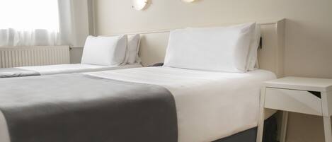 A hotel room with two beds, a bedside table, and a window with curtains.