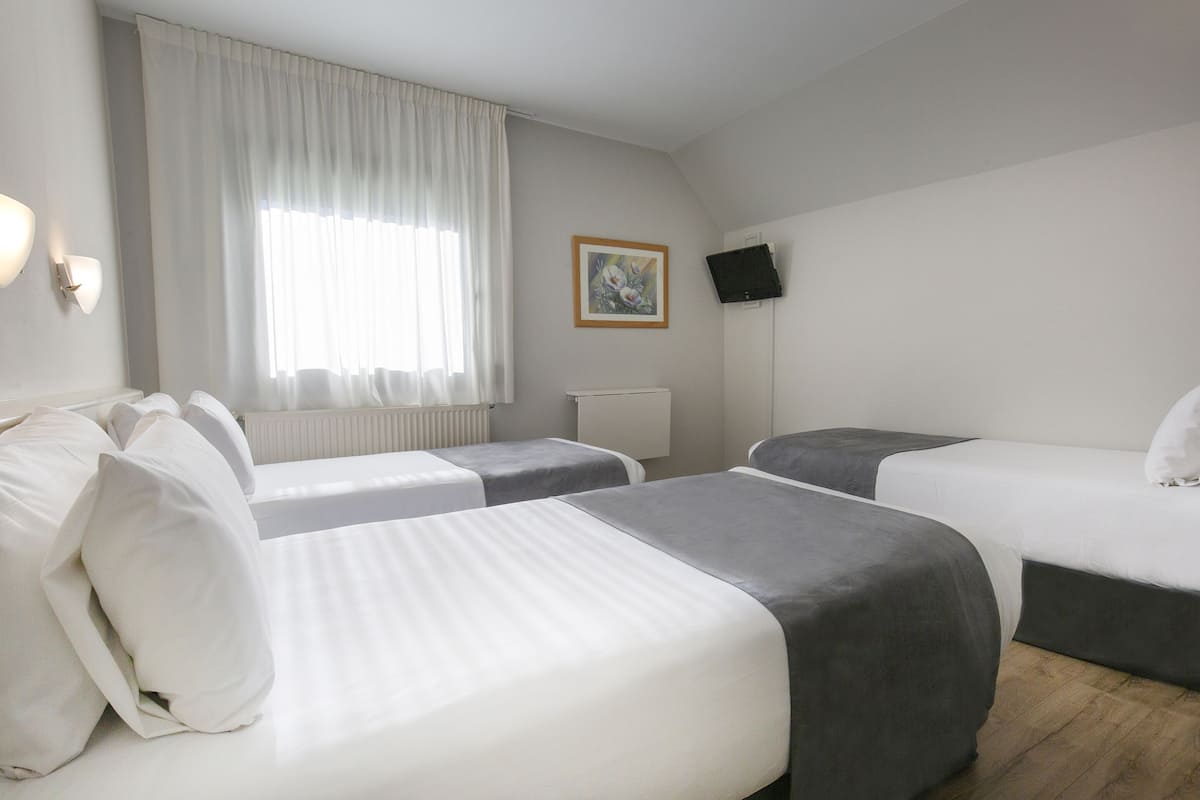 Une chambre d’hôtel avec deux lits, une fenêtre avec des rideaux, un téléviseur fixé au mur et un radiateur.