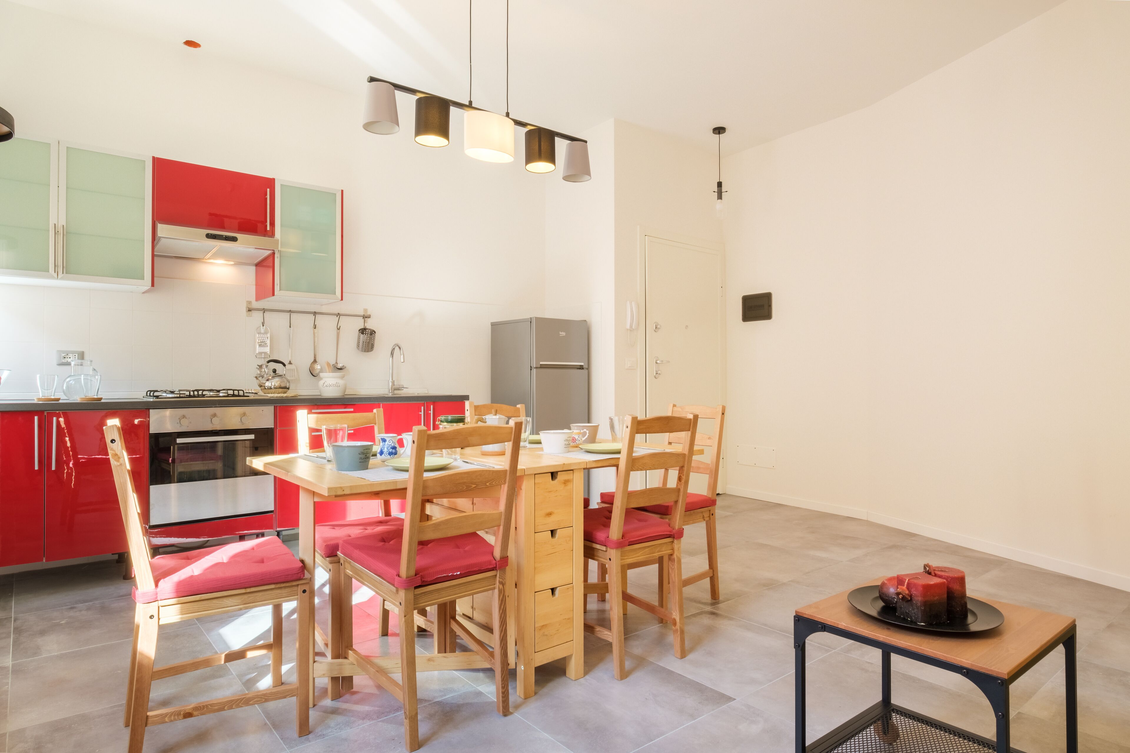 A modern kitchen with red cabinets, wooden chairs, and a dining table.