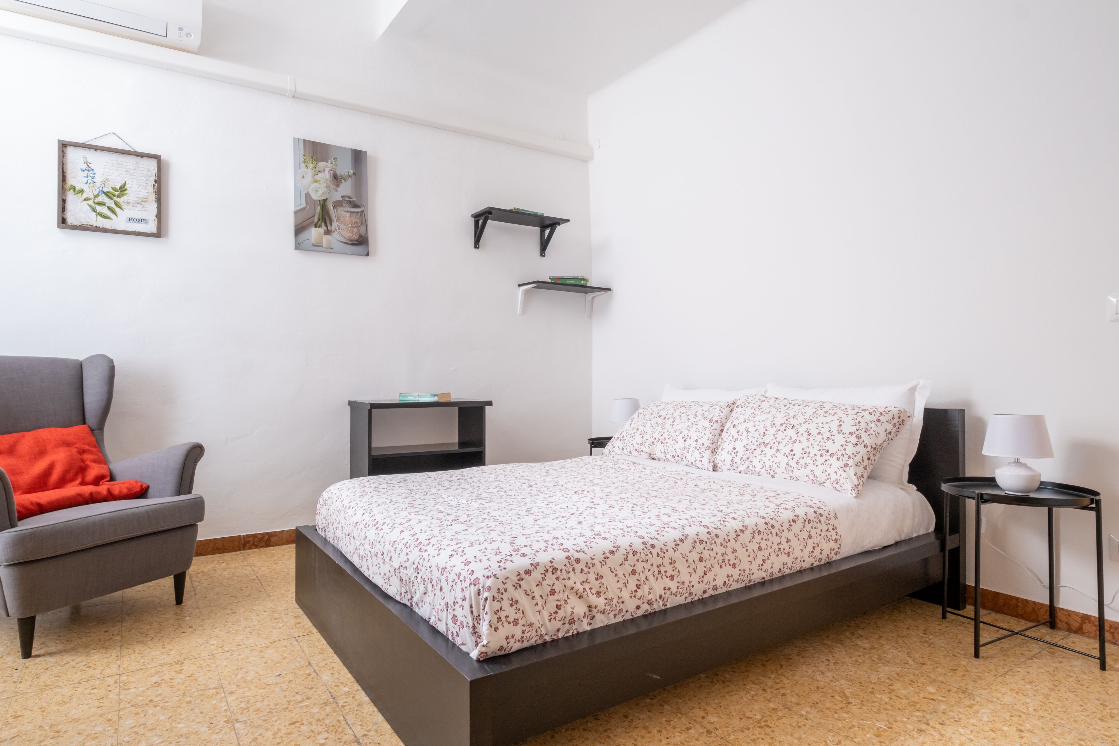 Une chambre moderne avec un lit, une chaise, une petite table et des étagères fixées au mur.