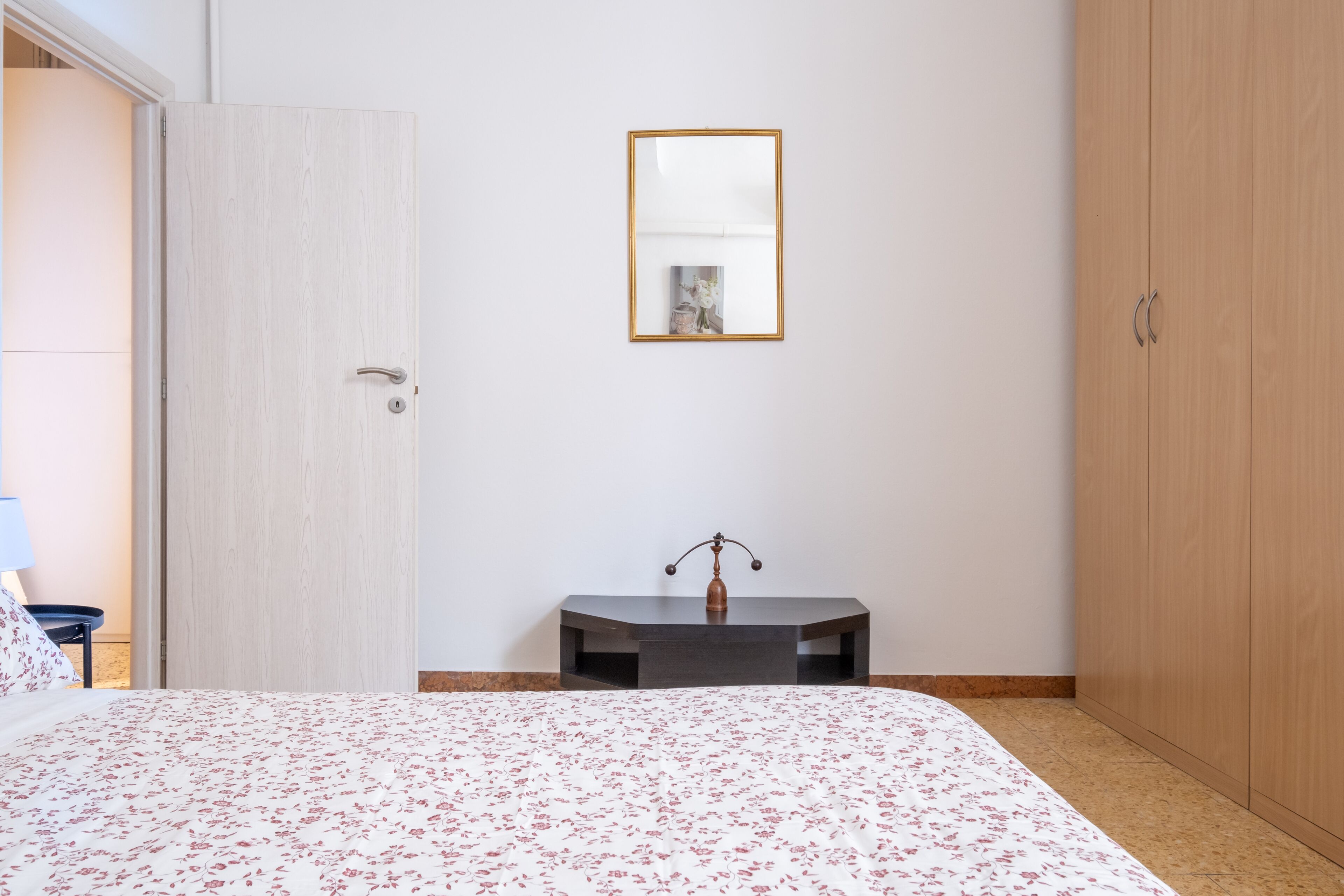 Quarto com cama, mesa de cabeceira, espelho, guarda-roupa e porta.