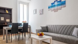Uma sala de estar com um sofá cinza, uma mesa de centro branca e um espaço de jantar com mesa e cadeiras.