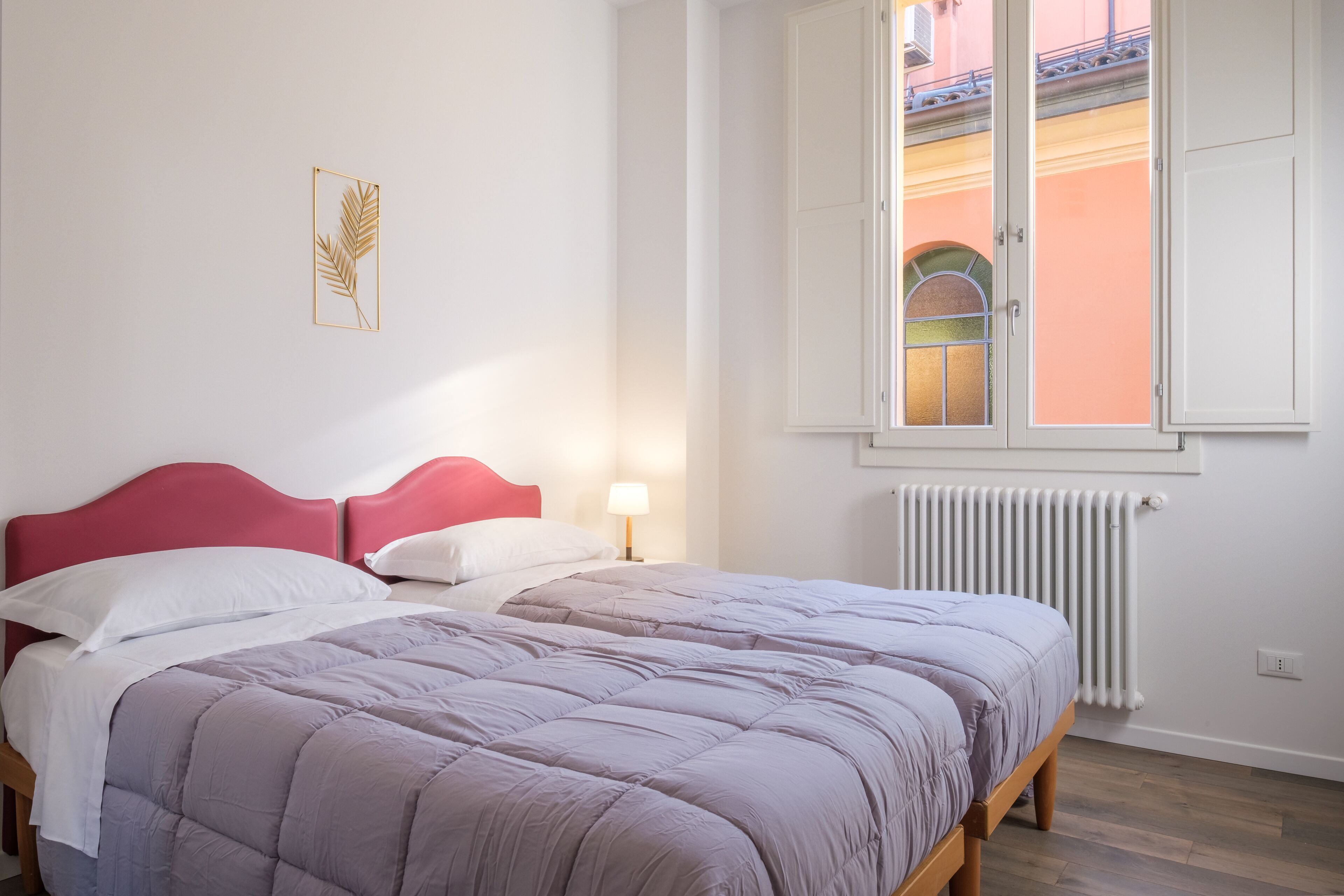 A bedroom with a bed, a window, a radiator, and a wall-mounted picture.