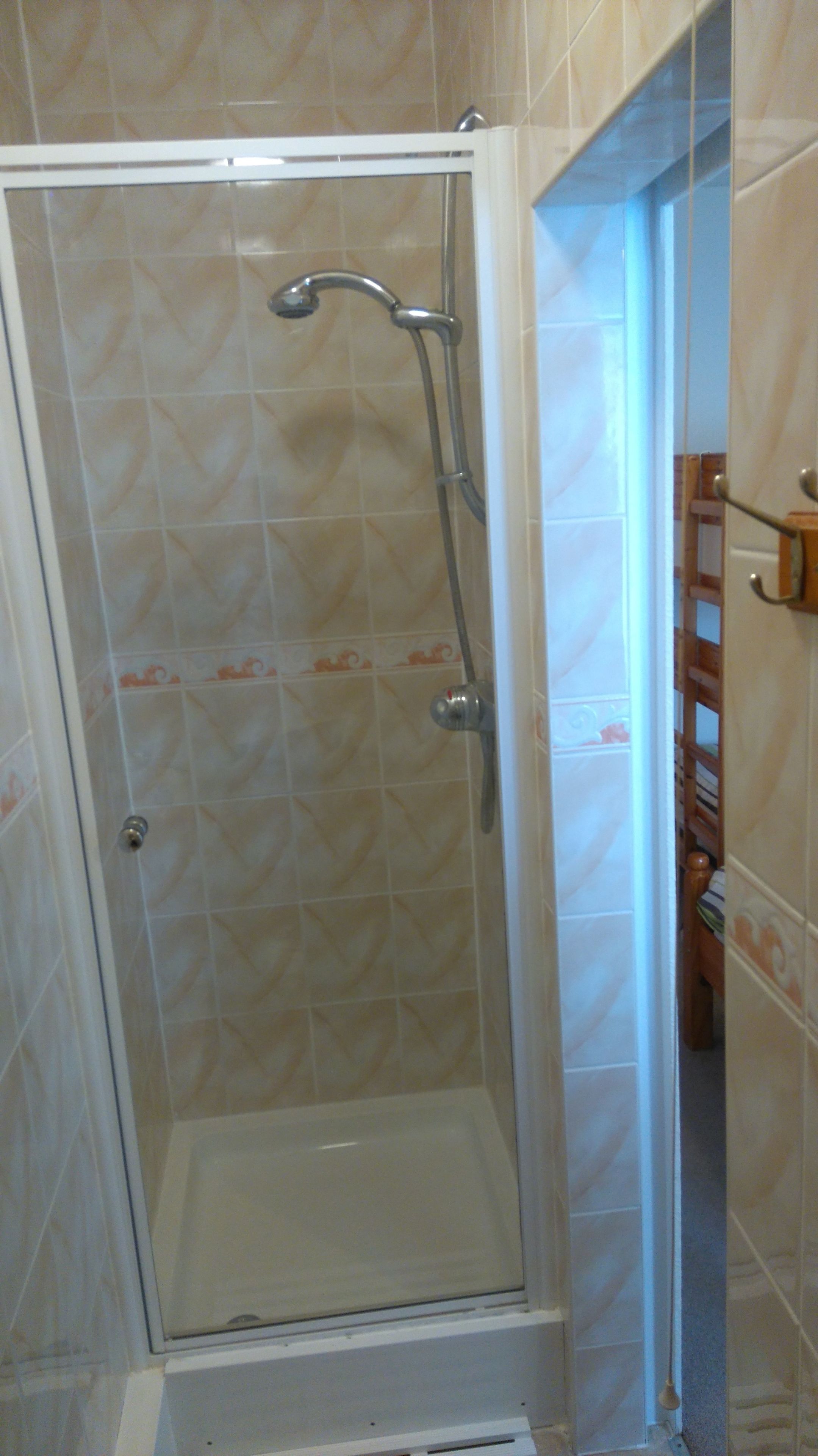 A glass-enclosed shower stall with a showerhead and control knob.