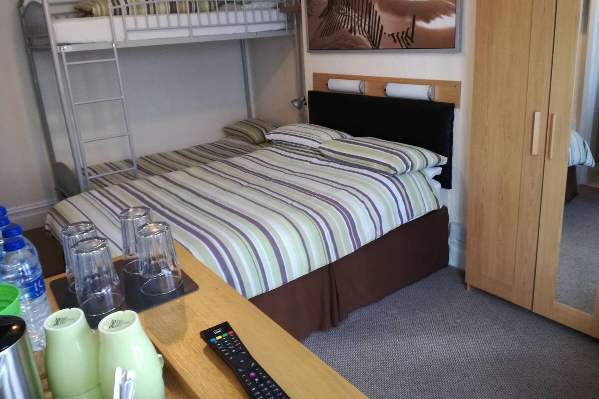 Uma cama beliche com colcha listrada, uma escrivaninha de madeira com controle remoto e um quadro pendurado na parede.
