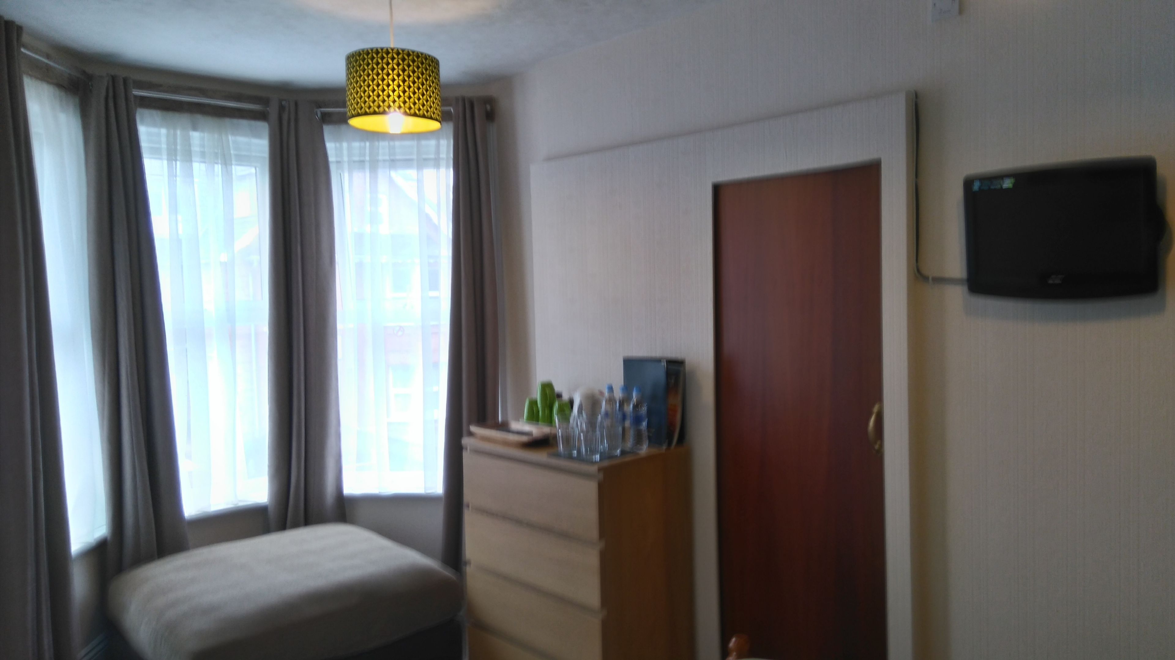 A hotel room with a bed, a dresser, a television on the wall, and a window with curtains.