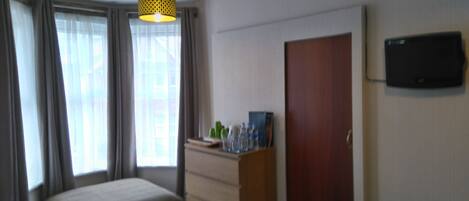 A hotel room with a bed, a dresser, a television on the wall, and a window with curtains.