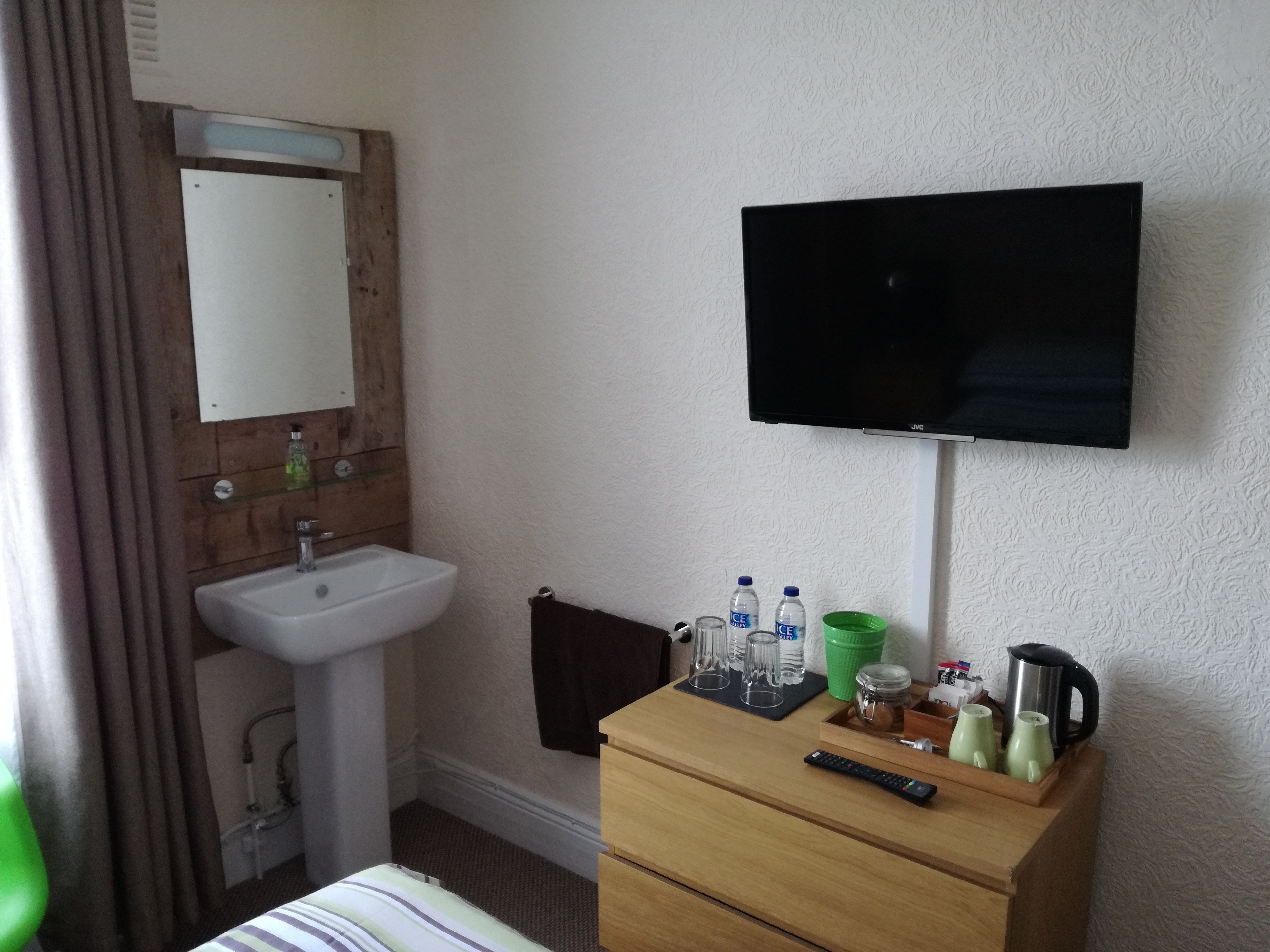 A hotel room with a wooden dresser, a TV mounted on the wall, a sink, and a bed with a striped bedspread.