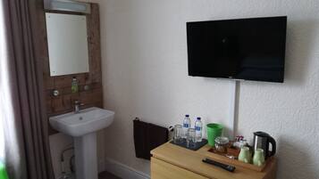 Una habitación de hotel con un aparador de madera, un televisor montado en la pared, un lavabo y una cama con colcha a rayas.