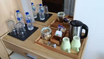 A hotel minibar with water bottles, glasses, a jar of cookies, a coffee maker, and tea cups.