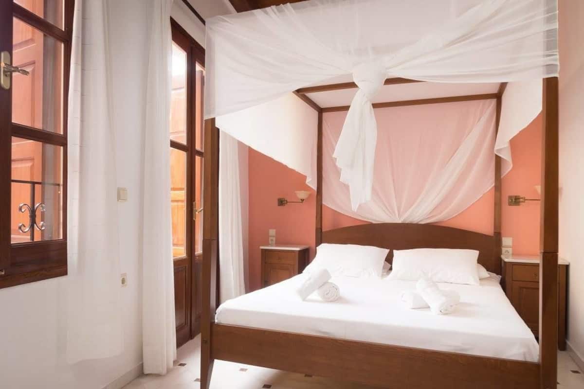 A four-poster bed with white linens and a canopy, wooden headboard, and bedside tables with lamps.