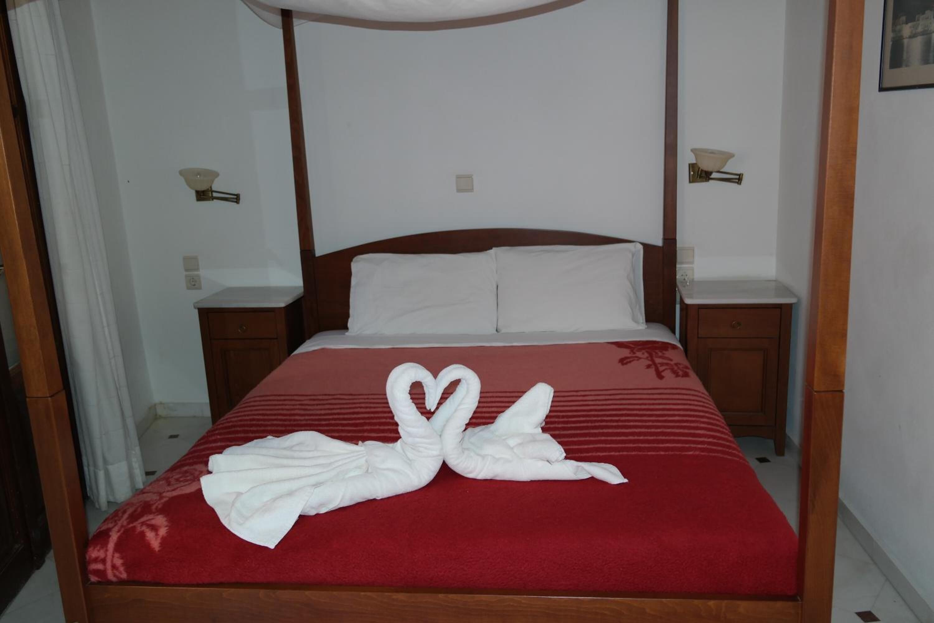 A neatly made bed with a red bedspread and white pillows, a wooden headboard, and two bedside tables with lamps.
