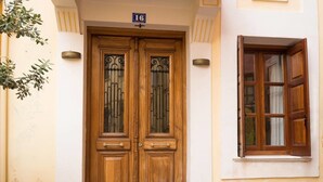 A wooden double door with a number plate, a window with wooden shutters, and a small plant to the left. - Xenon Apartments (Chania)