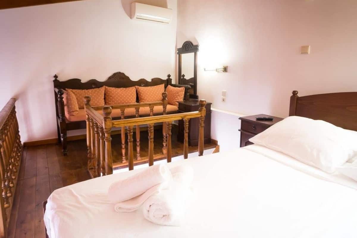 A bedroom with a wooden bed, a wooden bench with cushions, a bedside table, and a mirror.